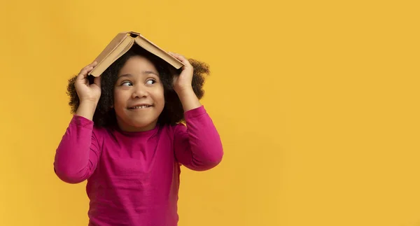 Edukacja i rozwój. Zabawna mała czarna dziewczyna ukrywa się pod otwartą księgą — Zdjęcie stockowe