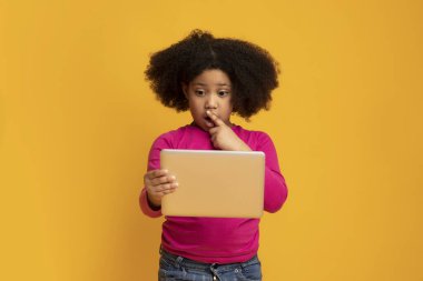 Şaşırmış küçük kız dijital tablet kullanıyor ve şaşkınlıkla ağzını açıyor.