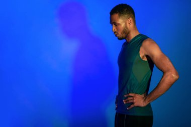 Spor kıyafetli adam nefes egzersizi yapıyor mavi arka planda duruyor.