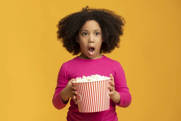 Chockad liten afrikansk flicka äter popcorn och öppna munnen i häpnad — Stockfoto