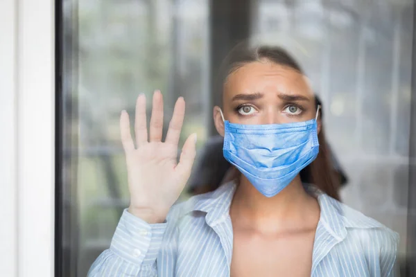 Meisje dragen masker kijken uit raam staan thuis — Stockfoto