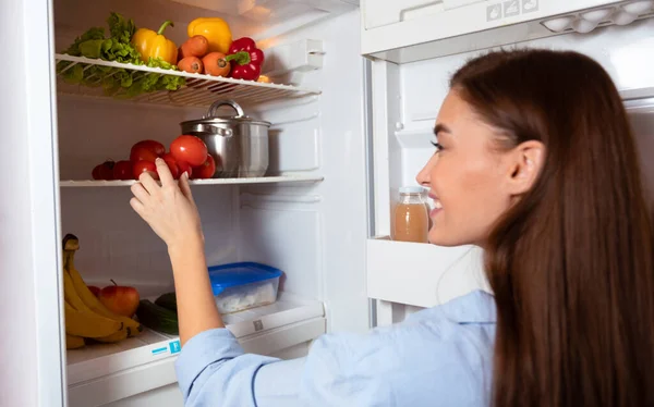 Menina feliz tomando vegetais orgânicos da geladeira em casa — Fotografia de Stock