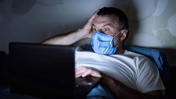 Przerażony facet w masce czyta wiadomości leżące w łóżku w domu — Zdjęcie stockowe