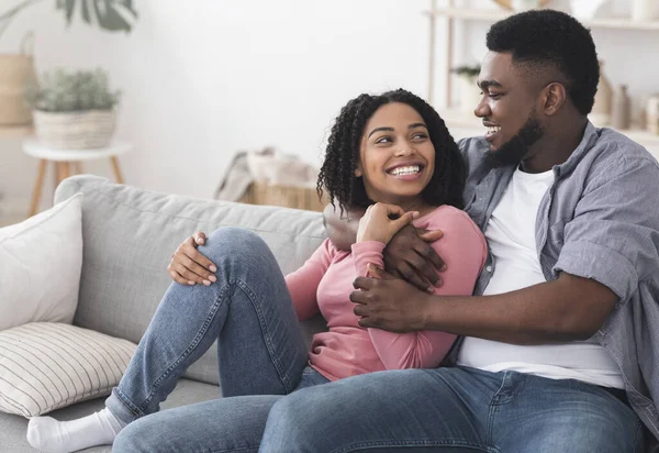 Romántica pareja negra relajándose en casa, abrazando y disfrutando del aislamiento juntos —  Fotos de Stock