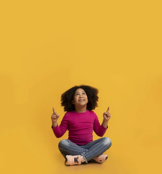 Menina preta sentada no chão e apontando para o espaço de cópia — Fotografia de Stock