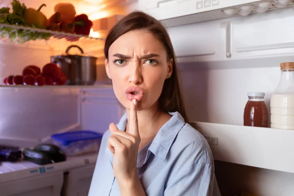 Angry hungry woman opening fridge late, gesturing on camera
