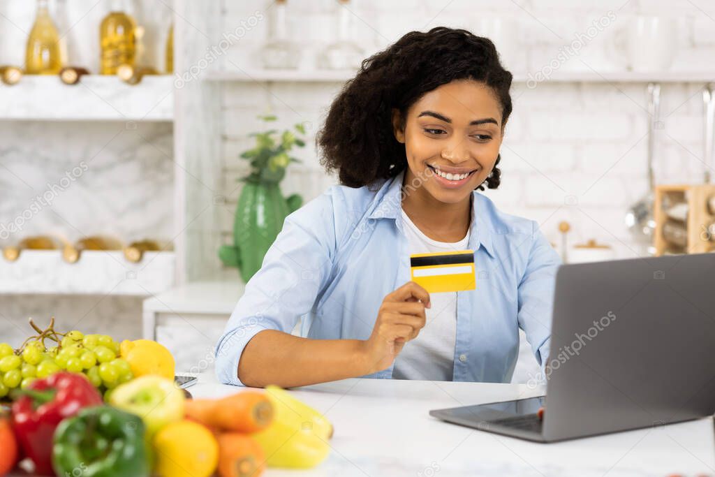 Afro girl using laptop and credit card in the kitchen