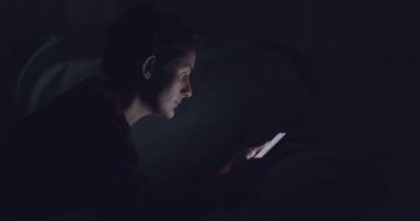 Cep telefonu olan bir kadın yatakta uzanıyor, geceleri geziniyor.