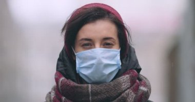 Koruyucu maske takan genç bir kadın şehirde tek başına duruyor.