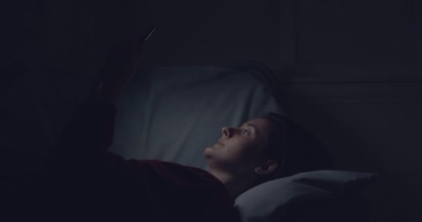 Junge Frau netzwerkelt am Smartphone, liegt nachts im Bett — Stockvideo