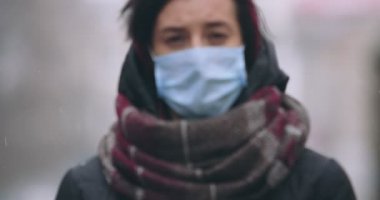 Koruyucu tıbbi maskeli kadın kamerada yavaşça yürüyor.