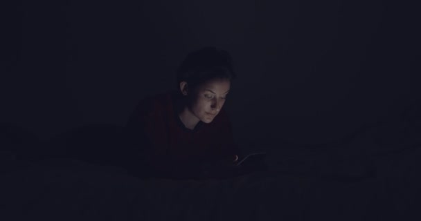 Jeune femme naviguant sur son téléphone portable, assise au lit la nuit — Video