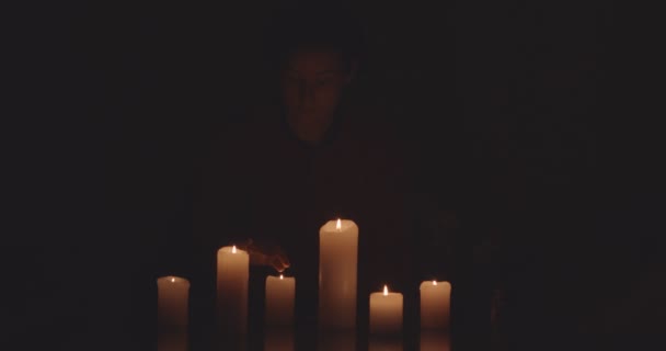 Mujer tocando fuego de velas encendidas en la oscuridad — Vídeos de Stock