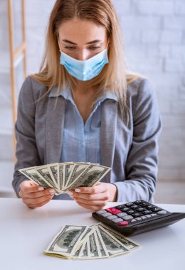 Woman in protecting mask counts dollars with calculator clipart