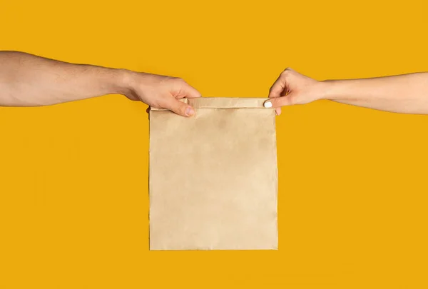 Comida para llevar. Entrega hombre dando bolsa de papel con espacio vacío para el diseño al cliente, fondo naranja — Foto de Stock