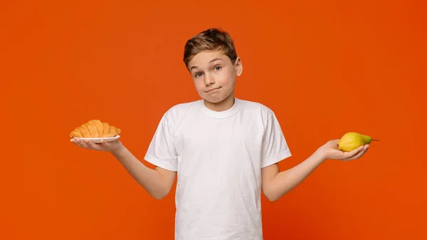 Töprengő tinédzser választás croissant és friss körte — Stock Fotó