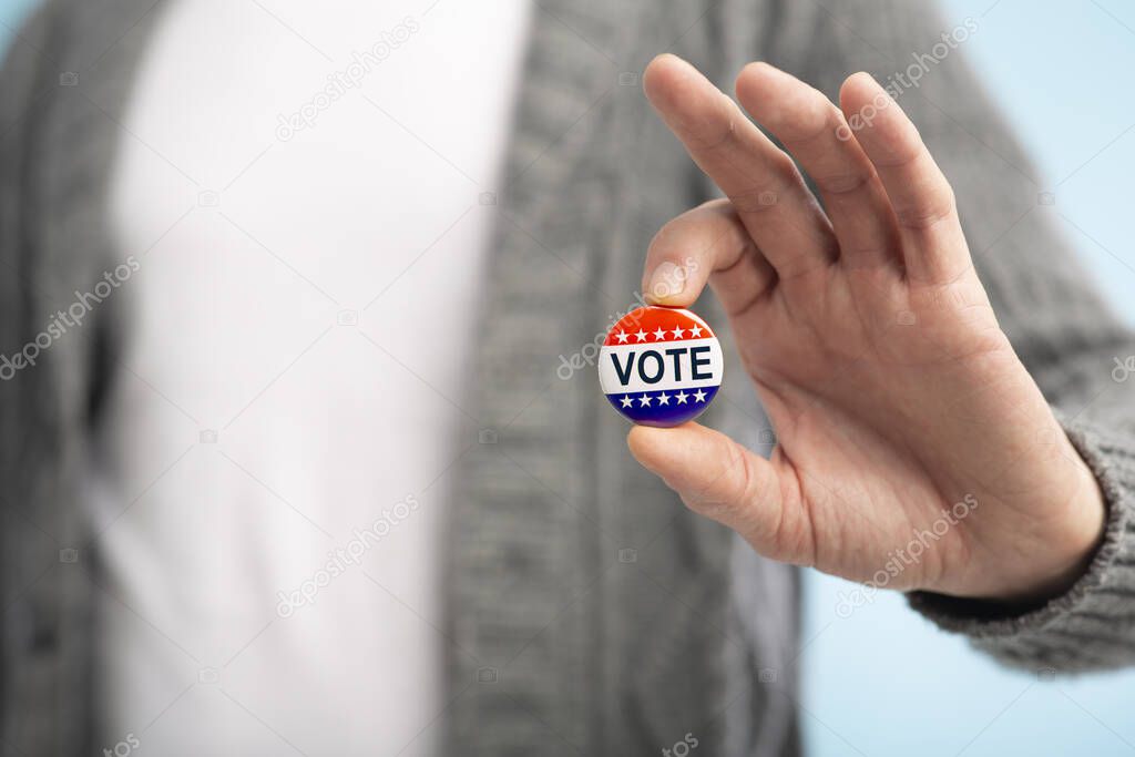 Man with vote pin in hand on blurred background