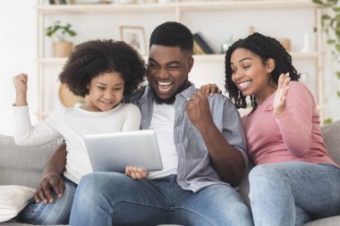 Neşeli siyah aile evde dijital tabletle başarıyı kutluyor
