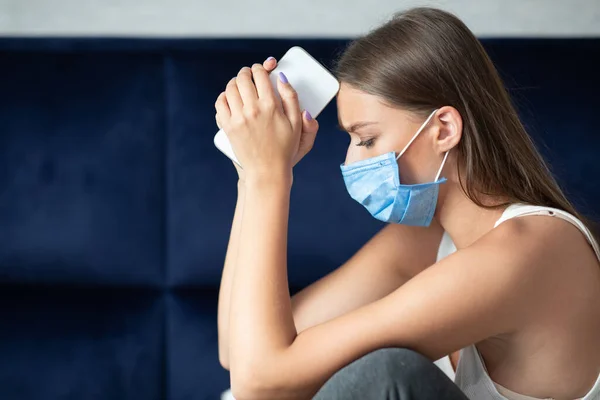 Vrouw in masker houden mobiele telefoon zittend op de bank thuis — Stockfoto