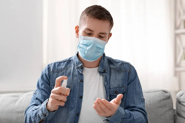Νεαρός άνδρας με προστατευτική μάσκα ψεκάζει απολυμαντικό στα χέρια — Φωτογραφία Αρχείου