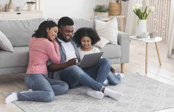 Preto pai, mãe, e pequena filha usando laptop em casa juntos — Fotografia de Stock