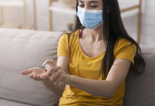 Гигиена во время эпидемии коронавируса. Тысячелетняя девочка в одноразовой маске наносит антисептик на руки дома — стоковое фото