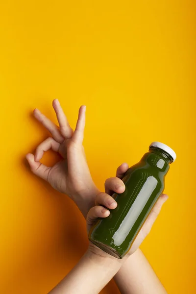 Femme main tenant bouteille avec smoothie vert de désintoxication sur jaune — Photo