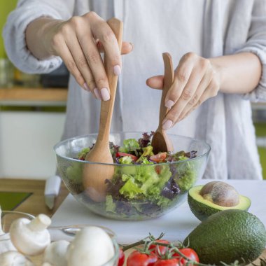 Ev hanımı salata yapıyor ve ahşap kaşıklarla karıştırıyor.
