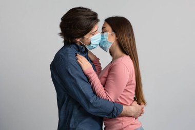 Romantik Karantina. Koruyucu tıbbi maskelerle öpüşen genç çift.