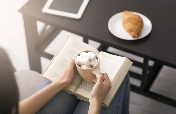 Passatempi di quarantena. Sopra vista di giovane ragazza con libro aperto e tazza di caffè con marshmallow a casa — Foto Stock