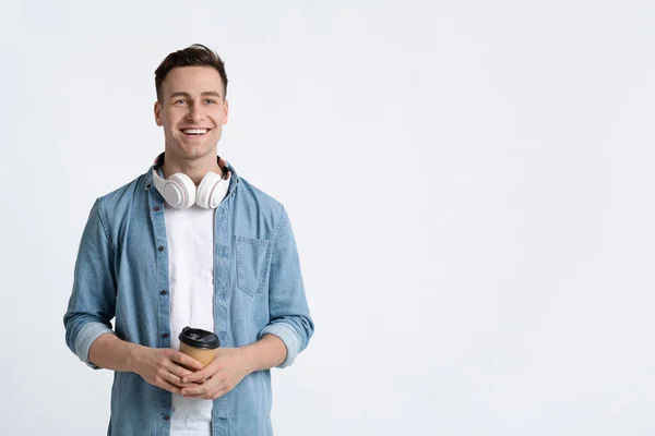 Chico con auriculares sonriendo y sostiene el café — Foto de Stock