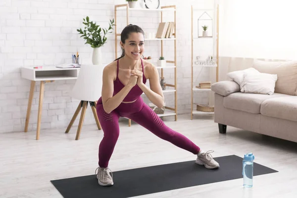 Stay home workout. Joyful millennial girl doing lunges on yoga mat in light room — Stock Photo, Image