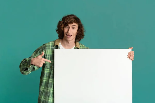 Cool millennial guy wijzend naar poster met lege ruimte voor uw advertentie op de turquoise achtergrond — Stockfoto