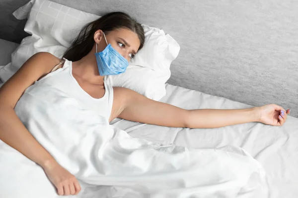 Ongelukkig meisje in masker liggen alleen in bed thuis — Stockfoto