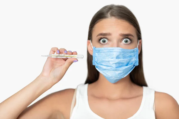 Bang vrouw in het masker met koorts tonen thermometer, witte achtergrond — Stockfoto
