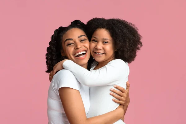 Niña negra abrazando a su madre posando sobre fondo rosa — Foto de Stock