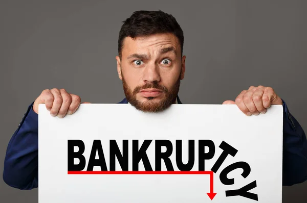 Şaşkın işadamının elinde BANKRUPTCY sözcüğü ve dinlenme grafiği olan gri bir arkaplan var. Kolaj — Stok fotoğraf