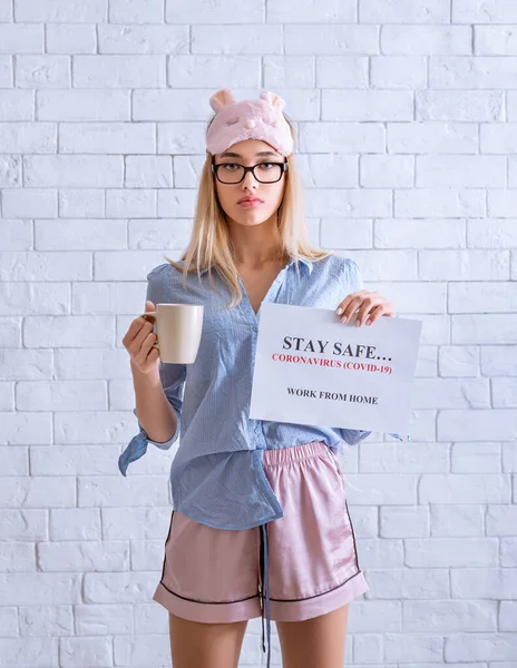 Woman in pajama with cup, holds inscription stay safe — Stock Photo, Image