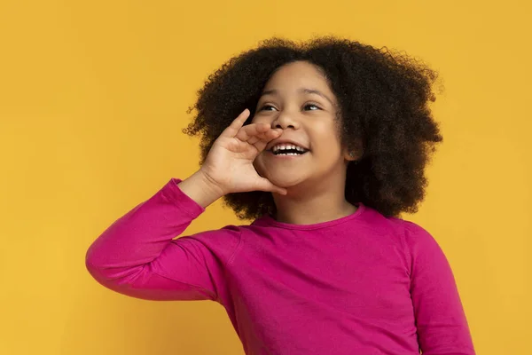 Extasiado bonito pequena criança negra de mão dada perto da boca, fazendo anúncio — Fotografia de Stock