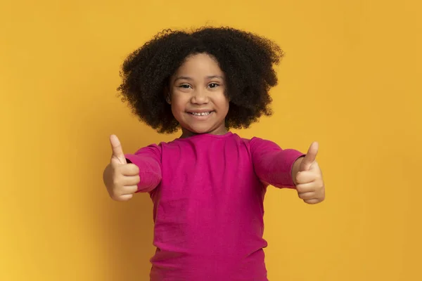 Menina preta bonito mostrando polegares para cima e sorrindo para a câmera — Fotografia de Stock