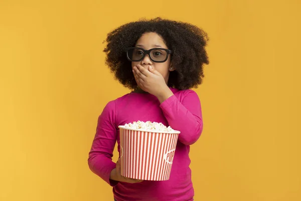 Menina africana chocada segurando pipocas e cobrindo a boca com a mão — Fotografia de Stock