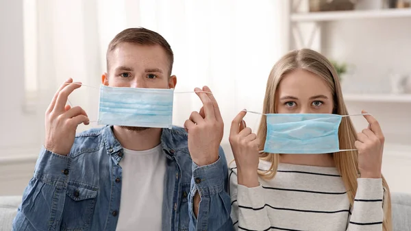 Young couple putting on protective medical masks at home — Stock Photo, Image