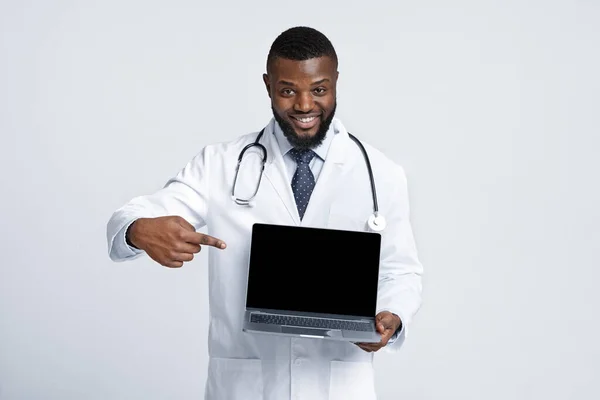 Czarny wesoły Doc wskazując na pusty ekran laptopa — Zdjęcie stockowe