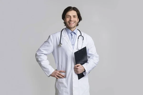 Zelfverzekerde glimlachende medische specialist met klembord poseren over lichte achtergrond — Stockfoto