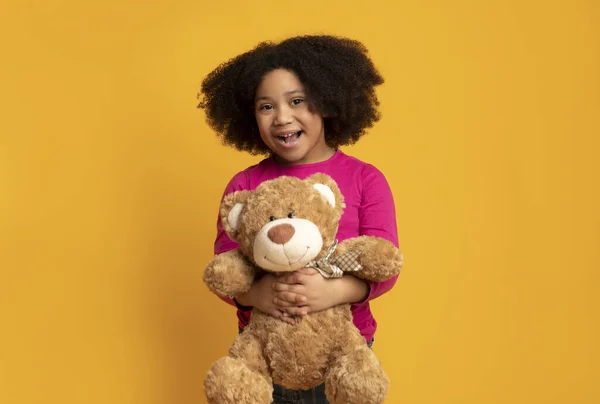 Gelukkig zwart meisje met Groot teddy beer over geel achtergrond — Stockfoto