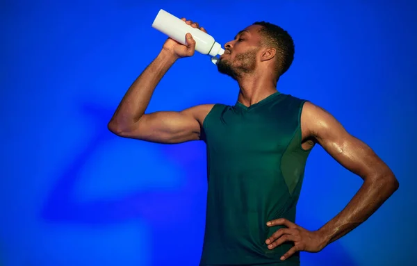 Negro deportivo chico beber agua después de ejercicio sobre azul fondo — Foto de Stock