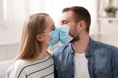 Koruyucu tıbbi maskeli bir çift evde öpüşüyor.