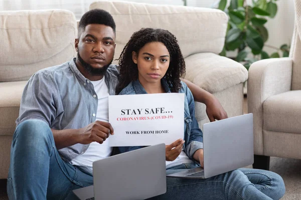 Negro millennial pareja trabajando remotamente en casa y sosteniendo cartel de advertencia — Foto de Stock
