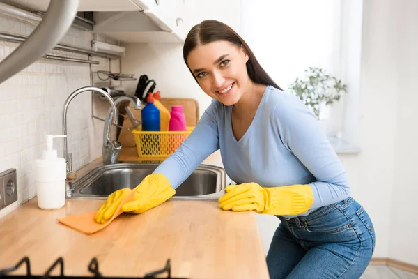 Dziewczyna sprzątanie mebli kuchennych z szmatą patrząc na aparat — Zdjęcie stockowe