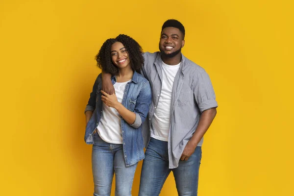 Smiling black man posing with girlfriend over yellow background in studio — Stock Photo, Image